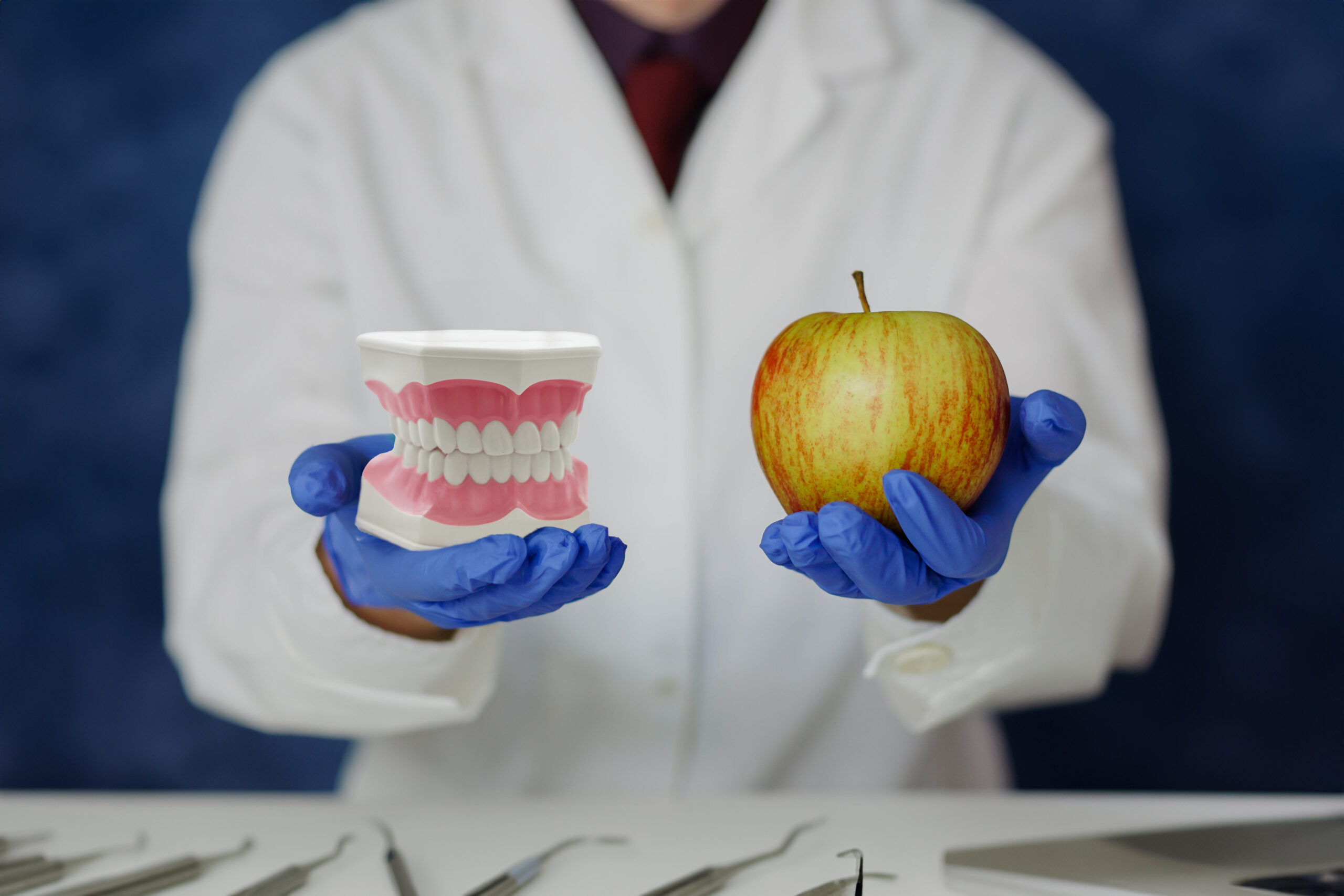 Hands of dentist showing apple and jaw teeth model for instruction how to caring healthy teeth for patient. Close up.