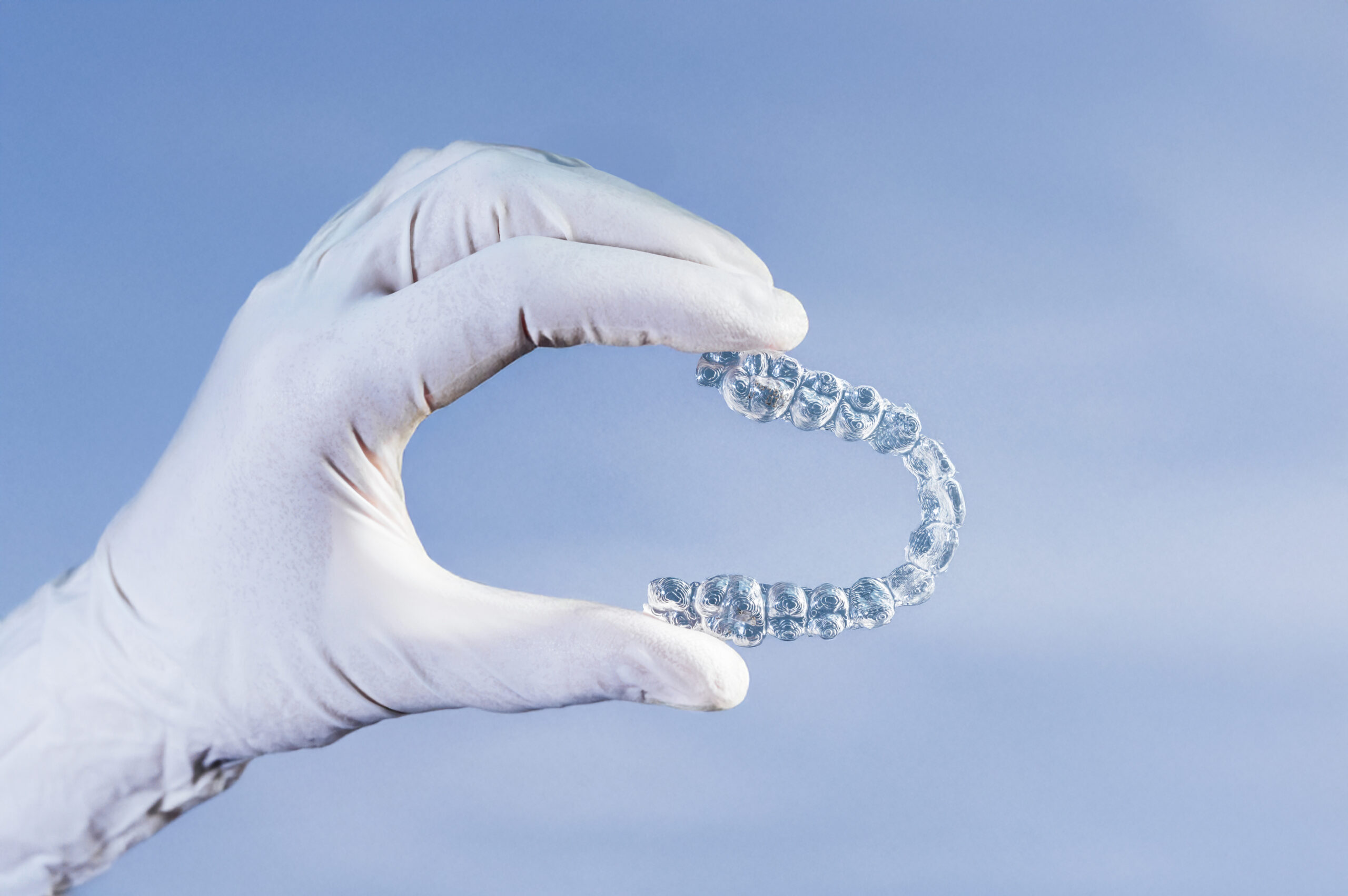 Doctor hand holding a clear dental aligner with the blue background