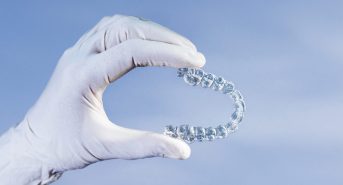 Doctor hand holding a clear dental aligner with the blue background