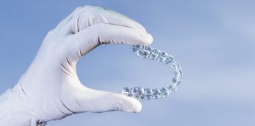 Doctor hand holding a clear dental aligner with the blue background