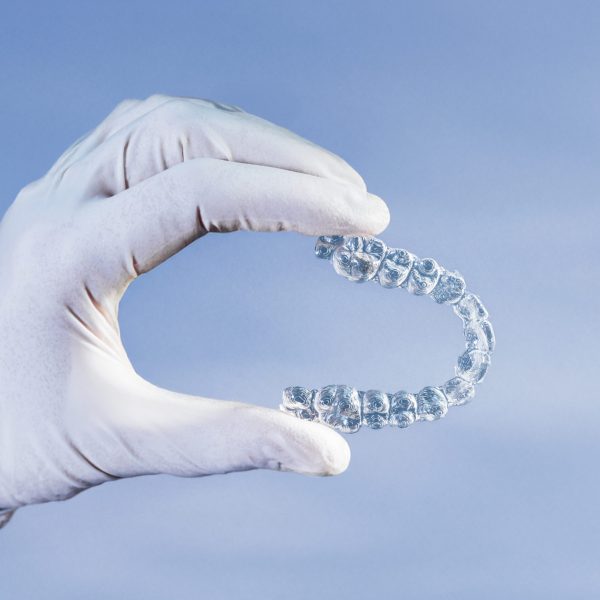 Doctor hand holding a clear dental aligner with the blue background